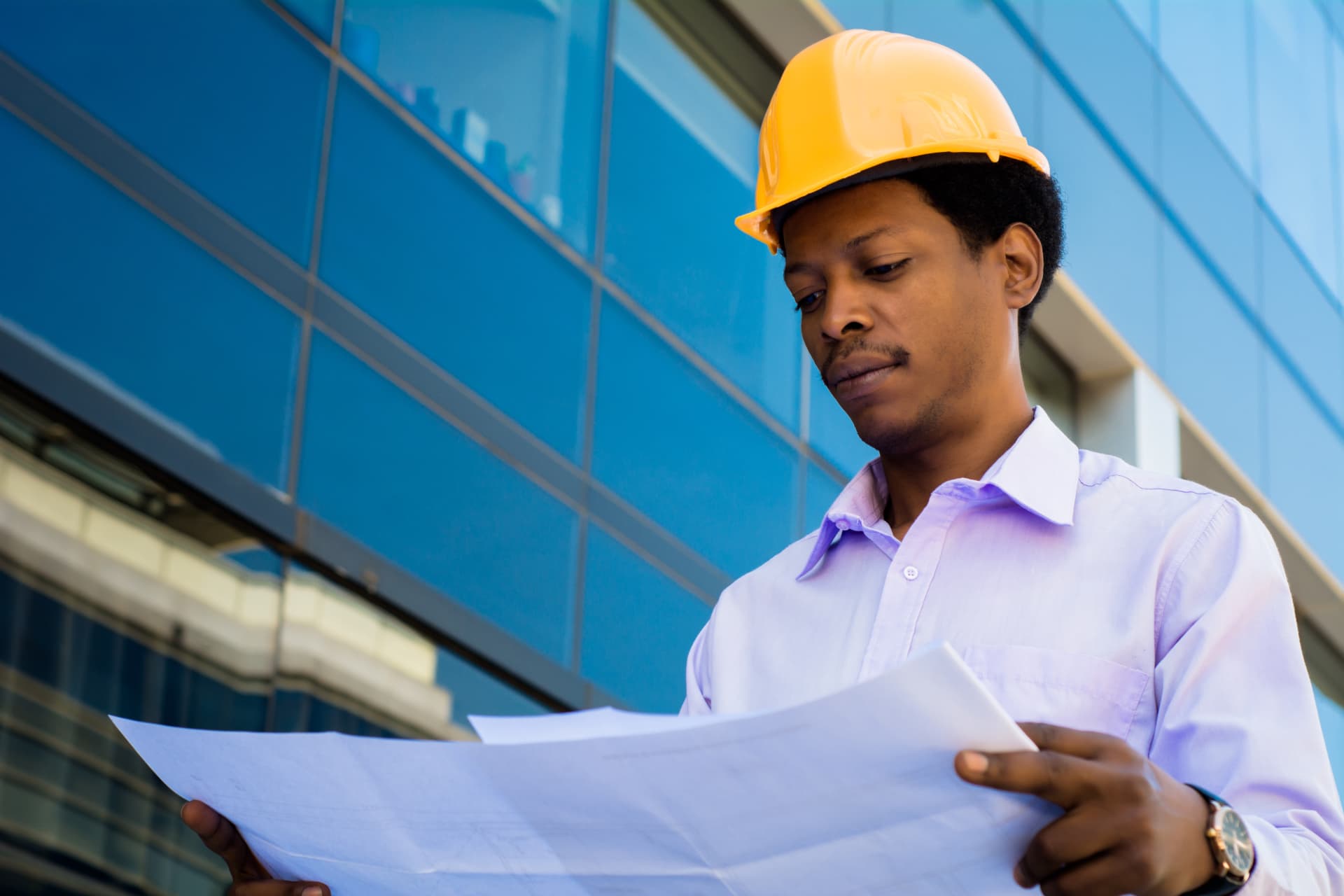 A professional architect in a hard hat reviewing blueprints outside a modern building